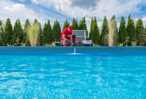 Pool technician performing maintenance on a residential swimming pool with tools and equipment beside the pool.